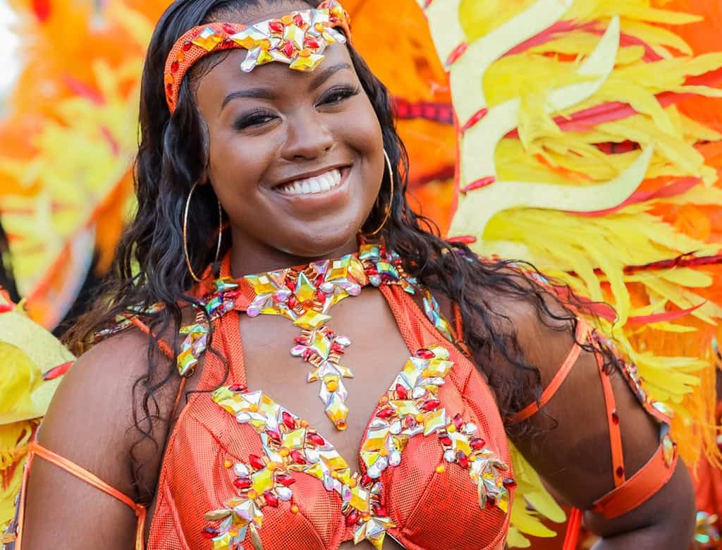 A person in a colorful outfit and headdress smiles at a USVI carnival