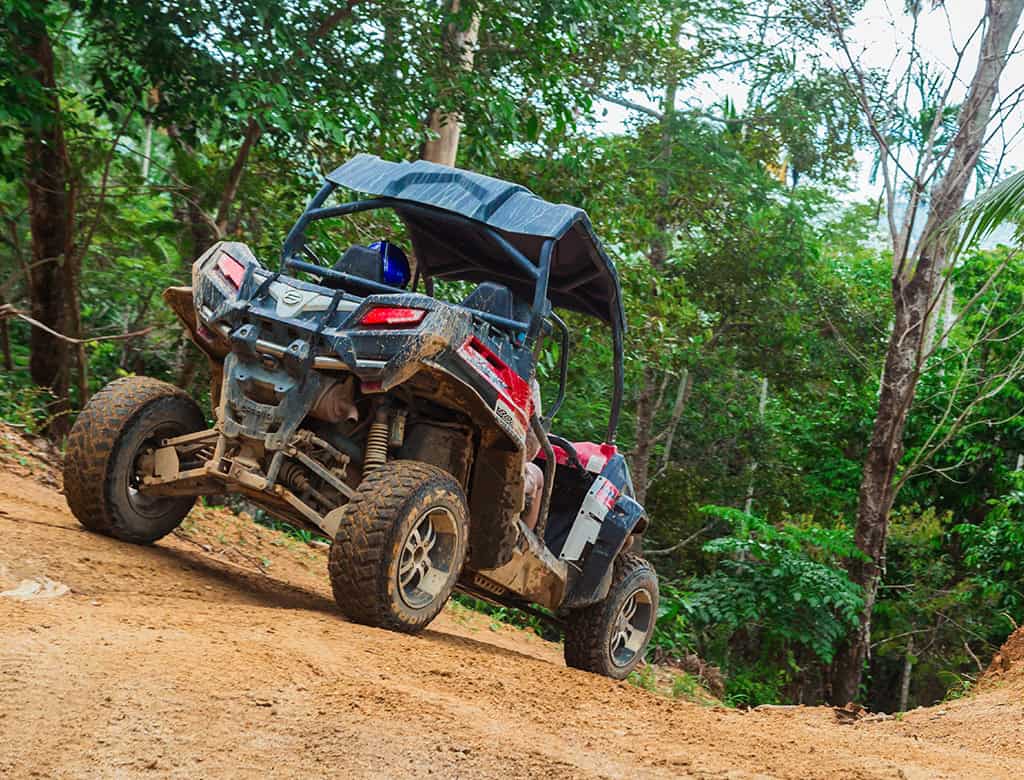 An ATV rides up a steep trail surrounded by lush vegetation