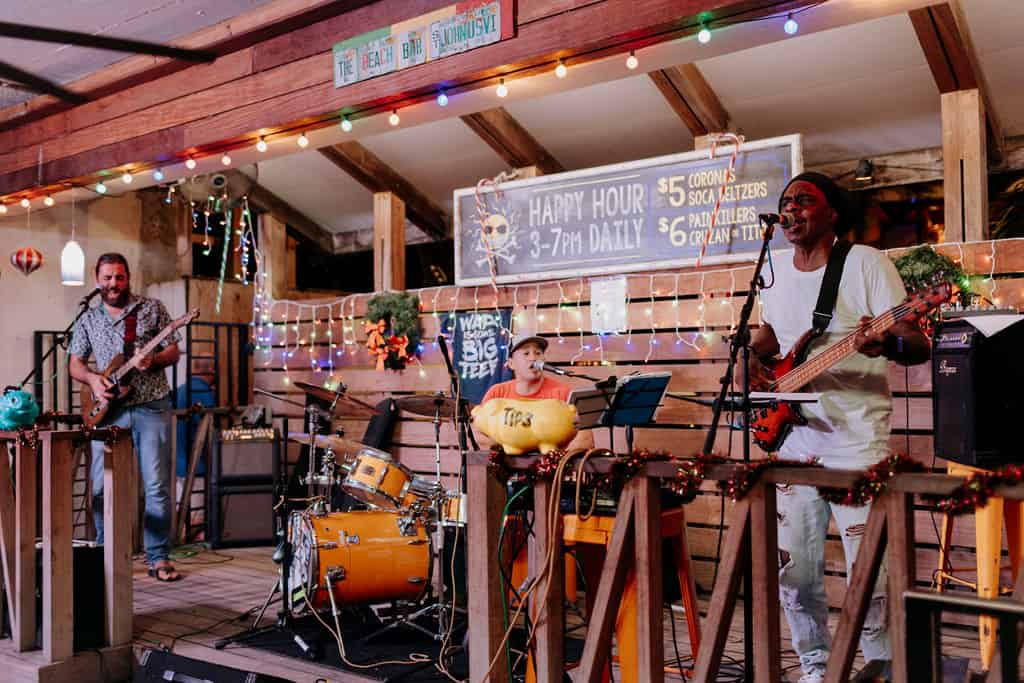 A band performs on a small stage surrounded by colorful string lights at The Beach Bar on St. John, USVI
