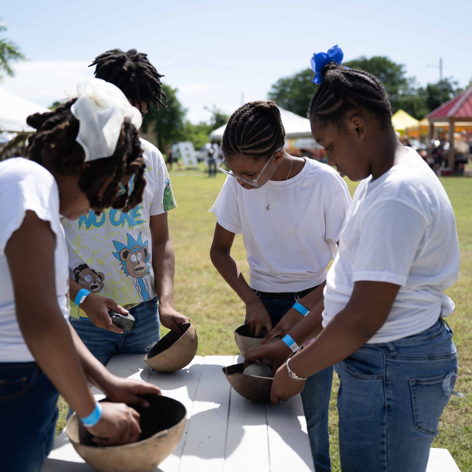 Four children stand around a white table outdoors, focused on cleaning or preparing items in large coconut bowls during the Crucian Coconut Festival on St. Croix. THIS IMAGE CAN BE USED ONLY IN CONJUNCTION WITH THAT FESTIVAL