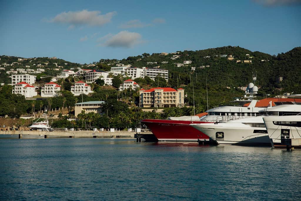 The Yacht Haven Grande marina with moored yachts and boats, with buildings on a hillside in the background under a clear blue sky in the USVI.