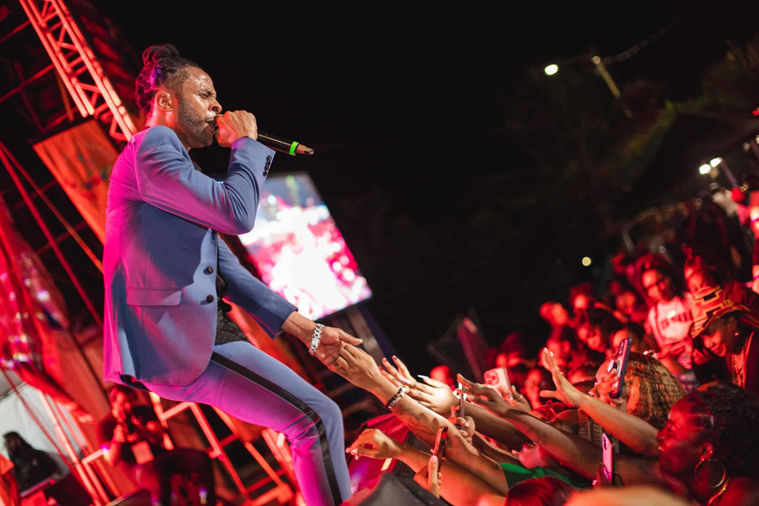 A performer in a blue suit sings passionately into a microphone on stage, reaching out to a crowd of fans under colorful lights at a night concert during the Crucian Christmas Festival in St. Croix, USVI.