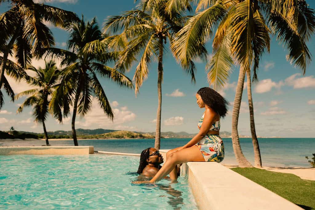 A couple in a pool surrounded by palm trees and blue skies by the ocean at Buccaneer Beach Resort, St. John, U.S. Virgin Islands