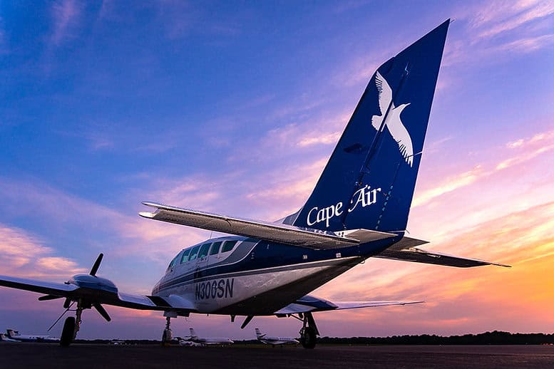 Small Cape Air plane parked on the tarmac during sunset, with the sky transitioning from blue to orange.