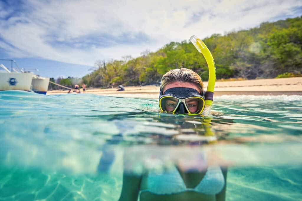 A person peeks over the water with a snorkeling mask by St. Croix. A beach is in the background.