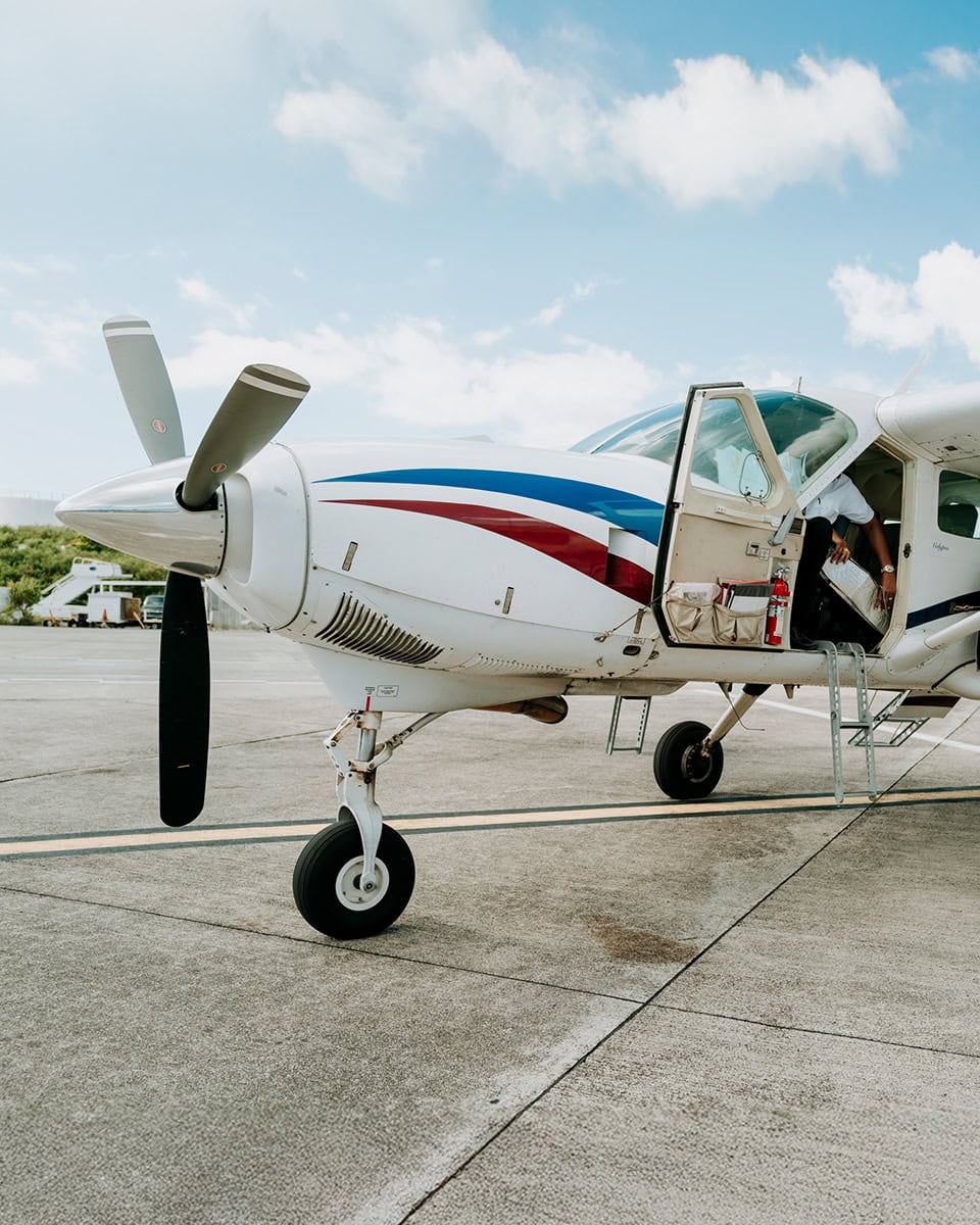 A small propeller airplane with an open door is parked on an airport tarmac under a partly cloudy sky.