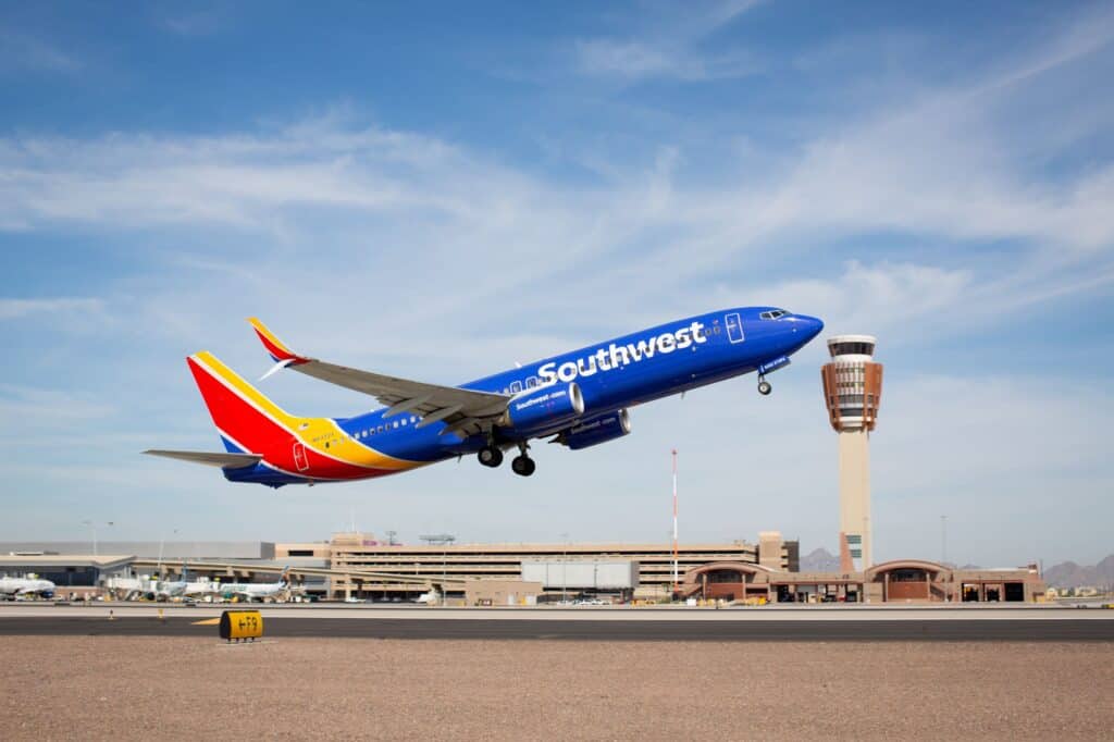 A Southwest Airlines plane taking off from an airport runway with the control tower and terminal buildings in the background.