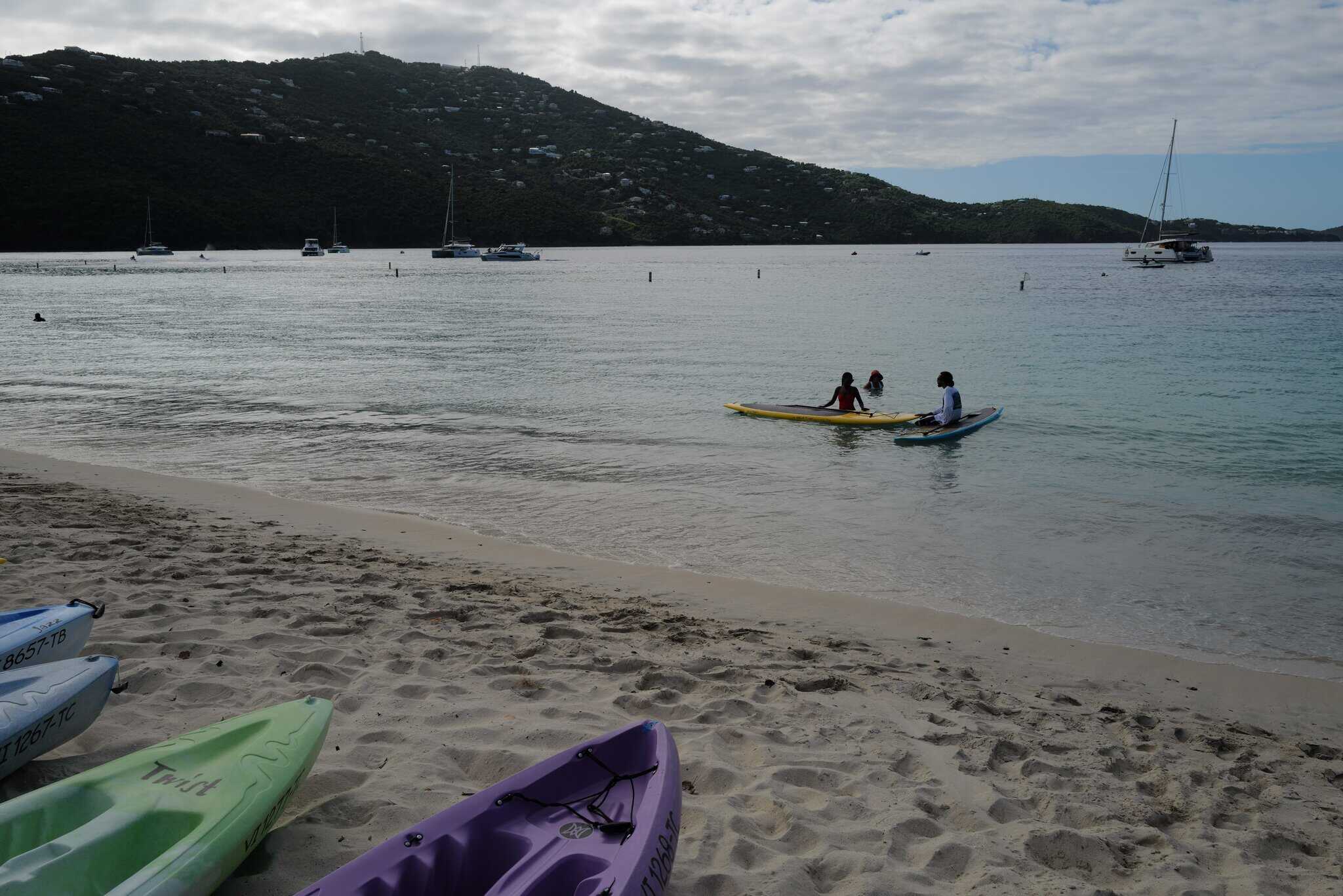 Kayaks on the shoreline with people kayaking in the water at Magens Bay Beach on St. Thomas in the USVI.