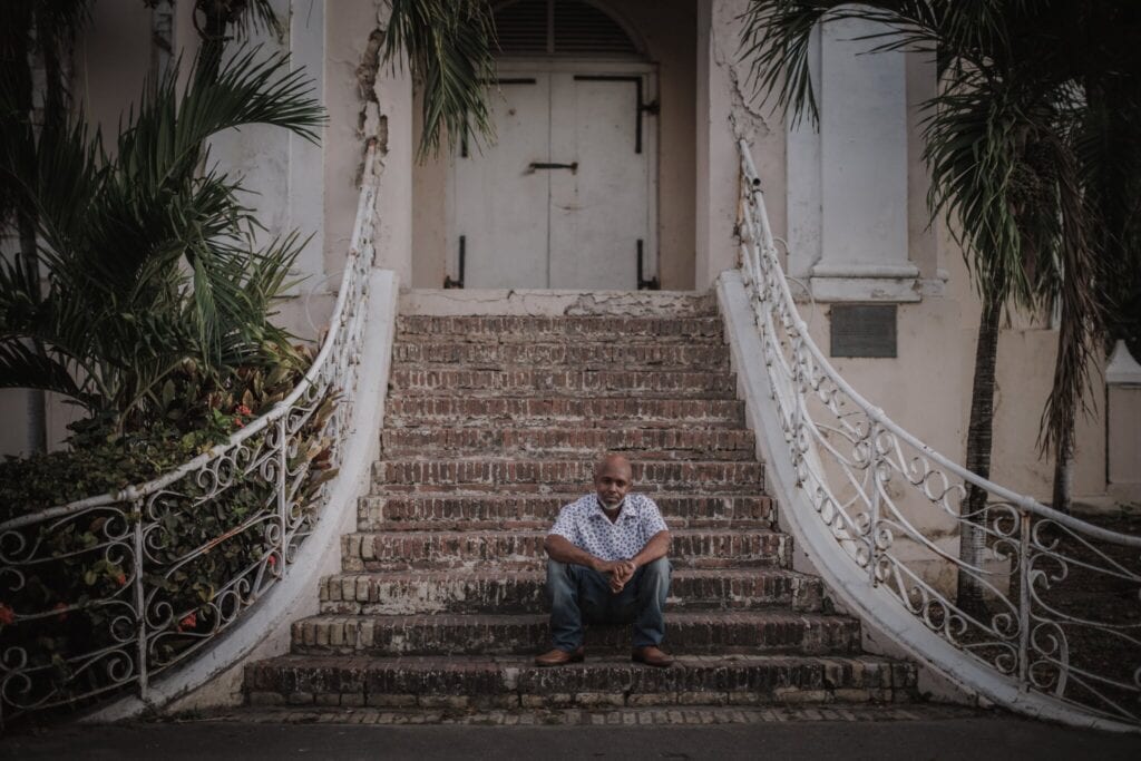 A man sits outside on stone steps leading up to the doors of the King Christian Hotel on St. Croix, U.S. Virgin Islands