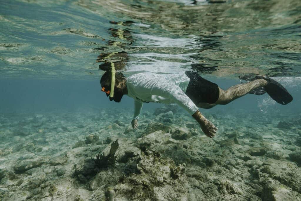 Person snorkeling underwater in Cinnamon Bay in St. John, U.S. Virgin Islands, near coral reefs, wearing a mask and swimwear, with sunlight filtering through the water.