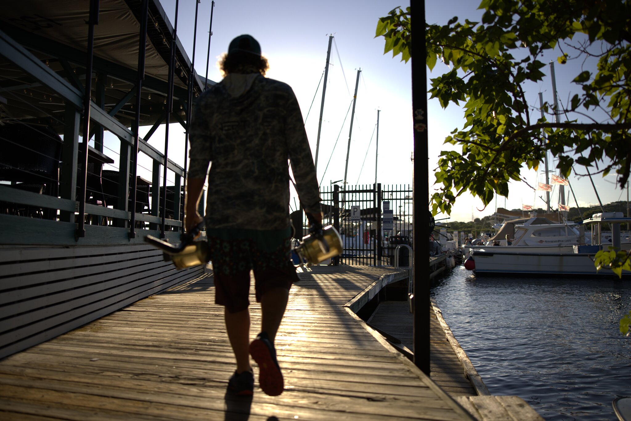 A person walks along a wooden dock by the water in Red Hook with boats and sunlight in the background on St. Thomas in the USVI.