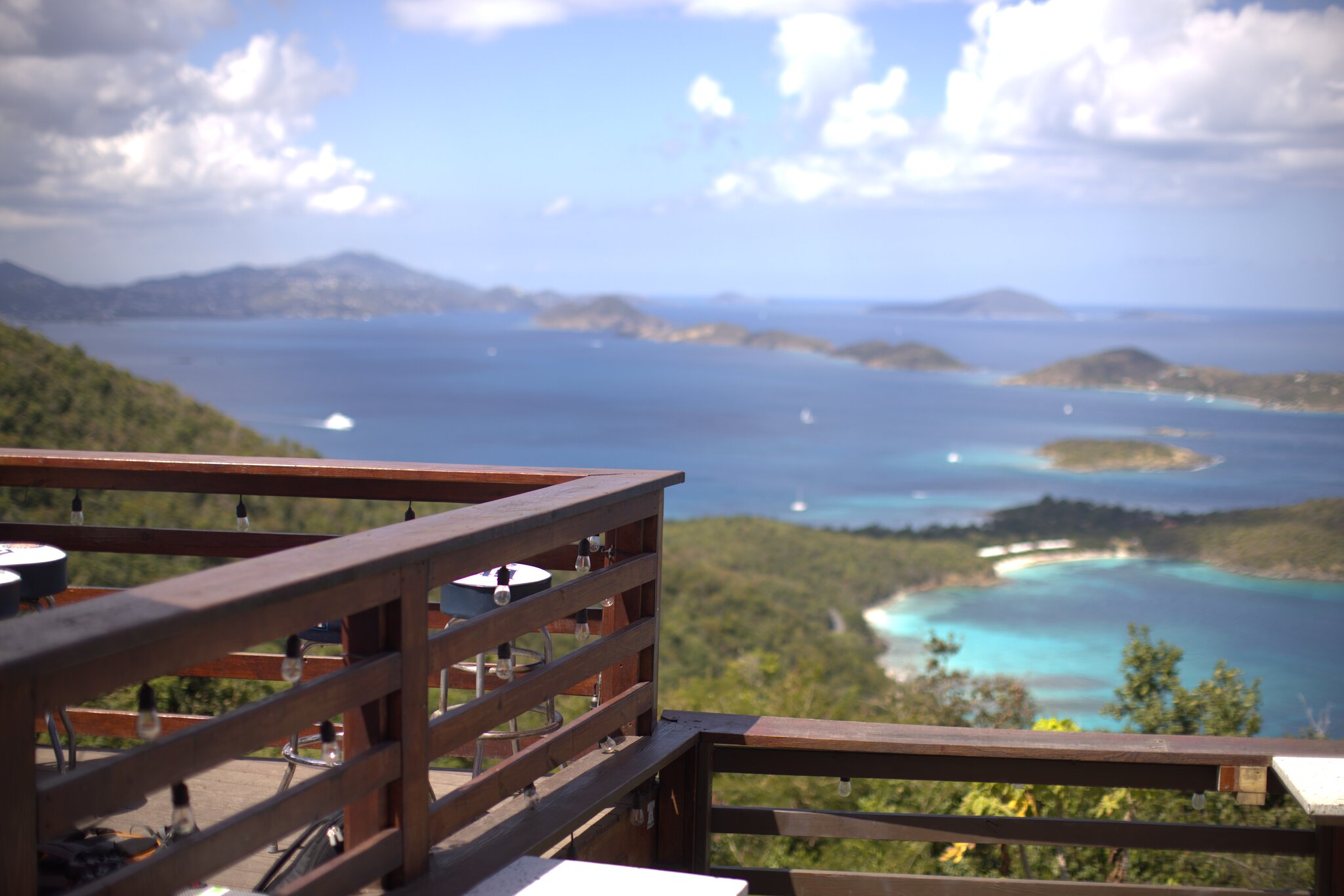 Wooden deck at The Windmill Bar on St. John in USVI overlooks a blue ocean, small islands, and green hills