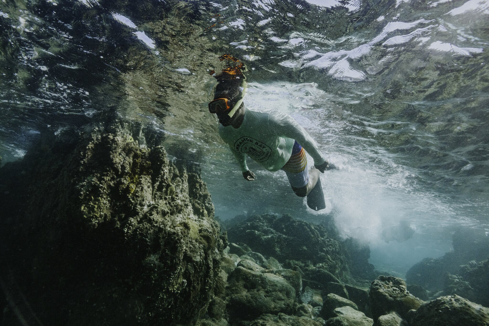 Person wearing a snorkel mask and swimwear swims underwater near rocky coral formations in clear, shallow water at Cinnamon Bay Beach on St. John in the U.S. Virgin Islands.
