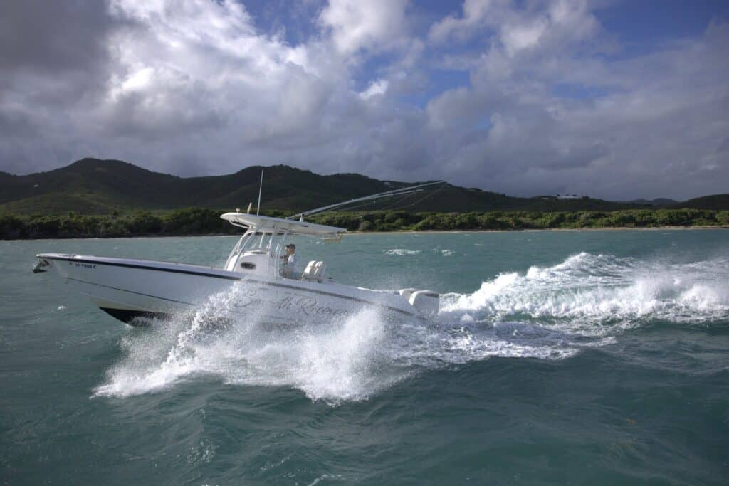 A white motorboat speeds across choppy water near a green, hilly coastline under a cloudy sky on St. Croix, USVI.