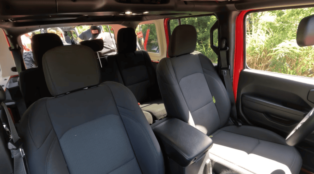 View of a red, four-passenger Jeep's interior with black seats, seen from the passenger side, with the doors open and people standing outside near the rear in the U.S. Virgin Islands.