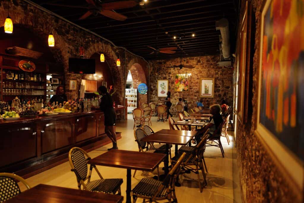 An interior view of Gladys' Cafe restaurant on St. Thomas, USVI, with a bar, stone walls, and bistro-style tables and chairs.