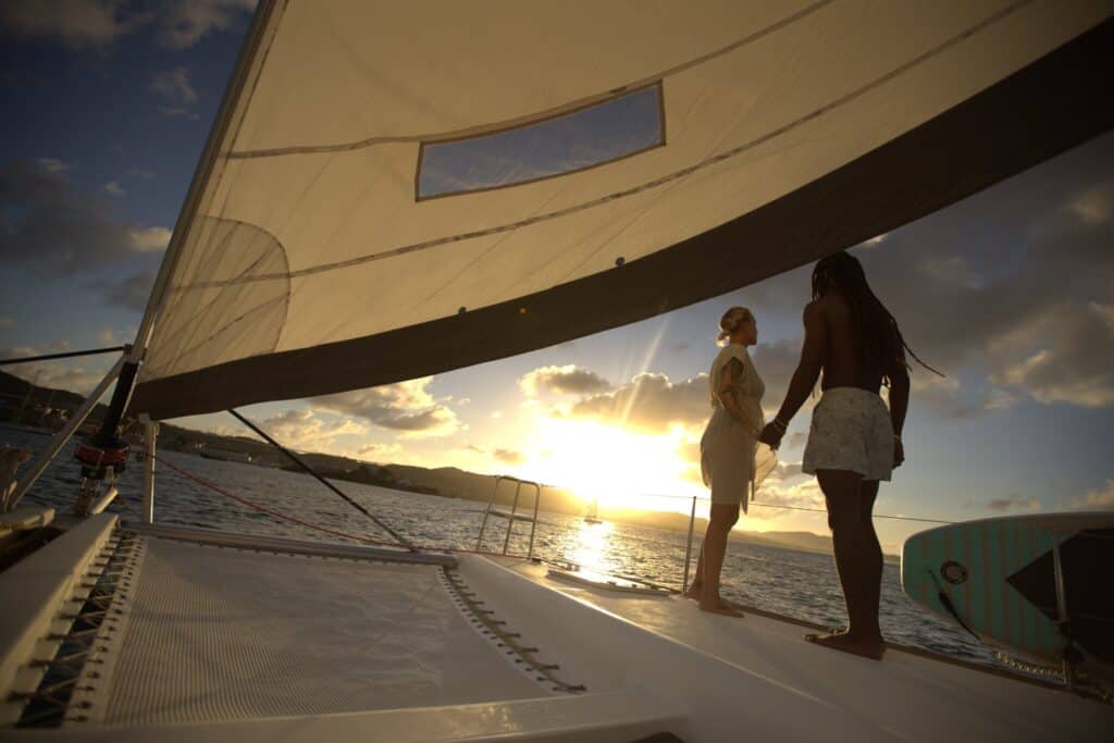 Two people stand hand-in-hand on the deck of a sailboat at sunset during a Sandy Toes Sailing sunset cruise on St. Croix, USVI.